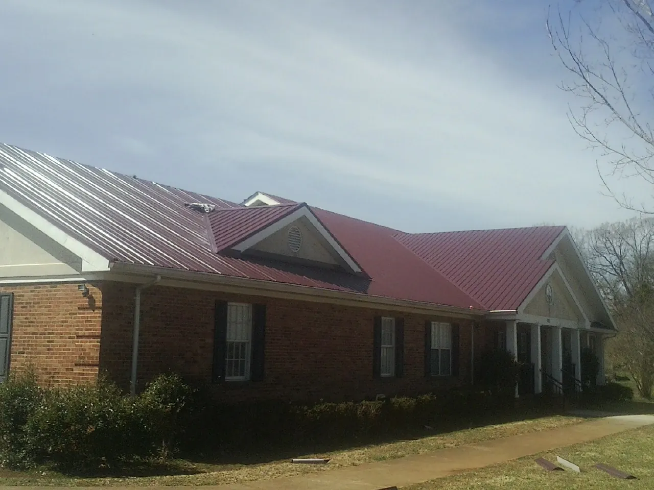 Red metal roof with gabled entries on a long brick building, from a Hail Damage Roof Repair job in West Blocton
