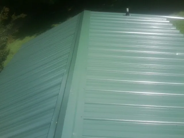 New green metal panels meeting at the ridge of a roof — Flat Roof Repair work by our crew in West Blocton