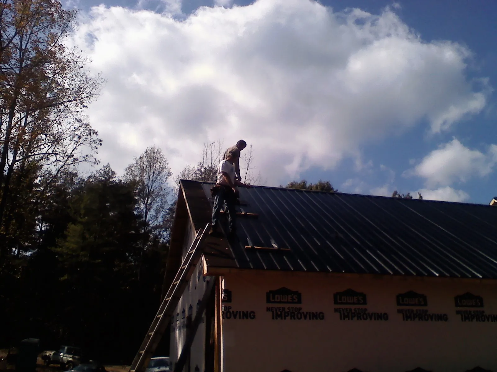 Roofer fastening dark metal panels high against a cloudy sky, from a Roof Inspection job in West Blocton