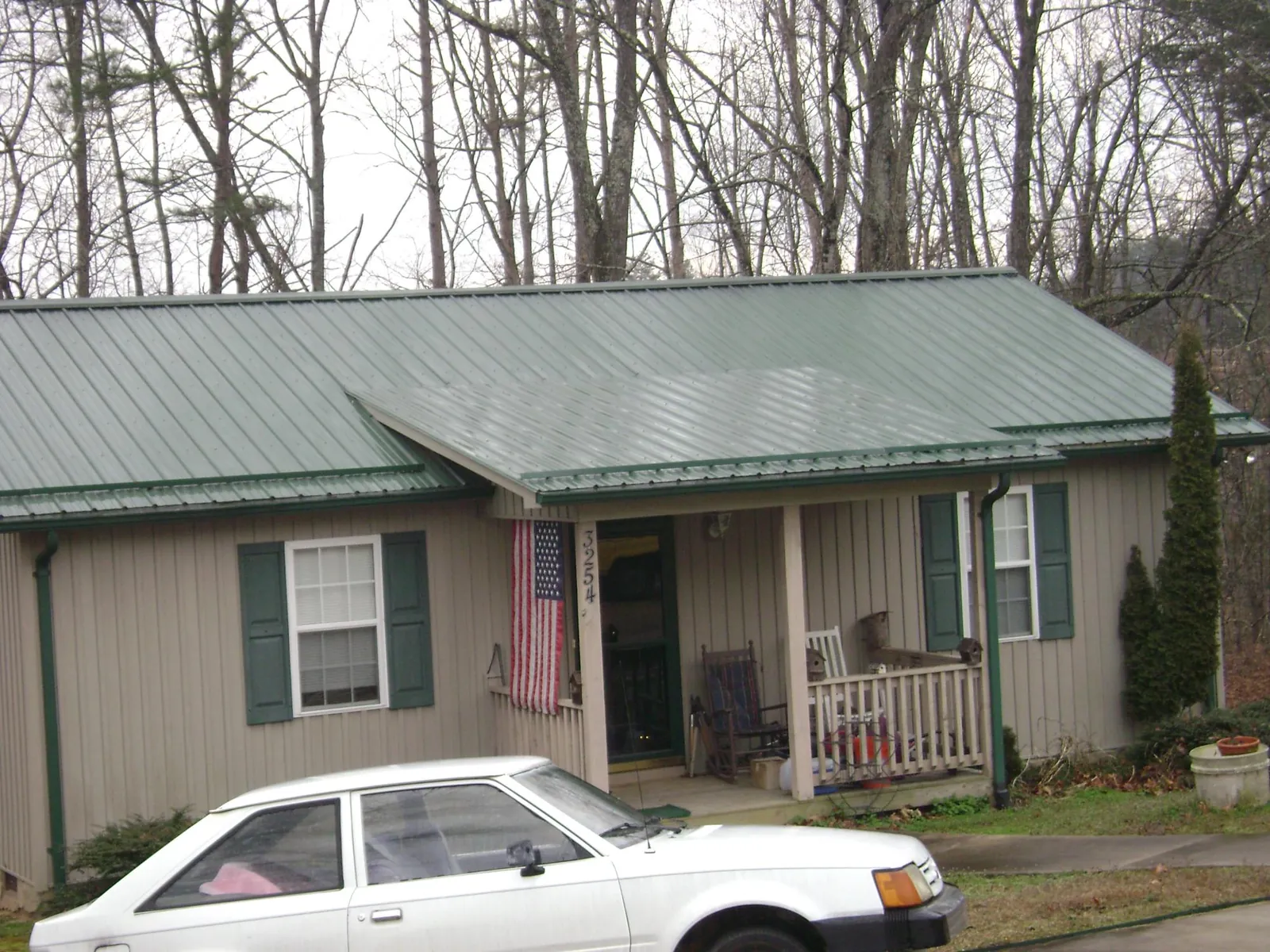 Green metal roof and front porch on a tan sided cottage in West Blocton