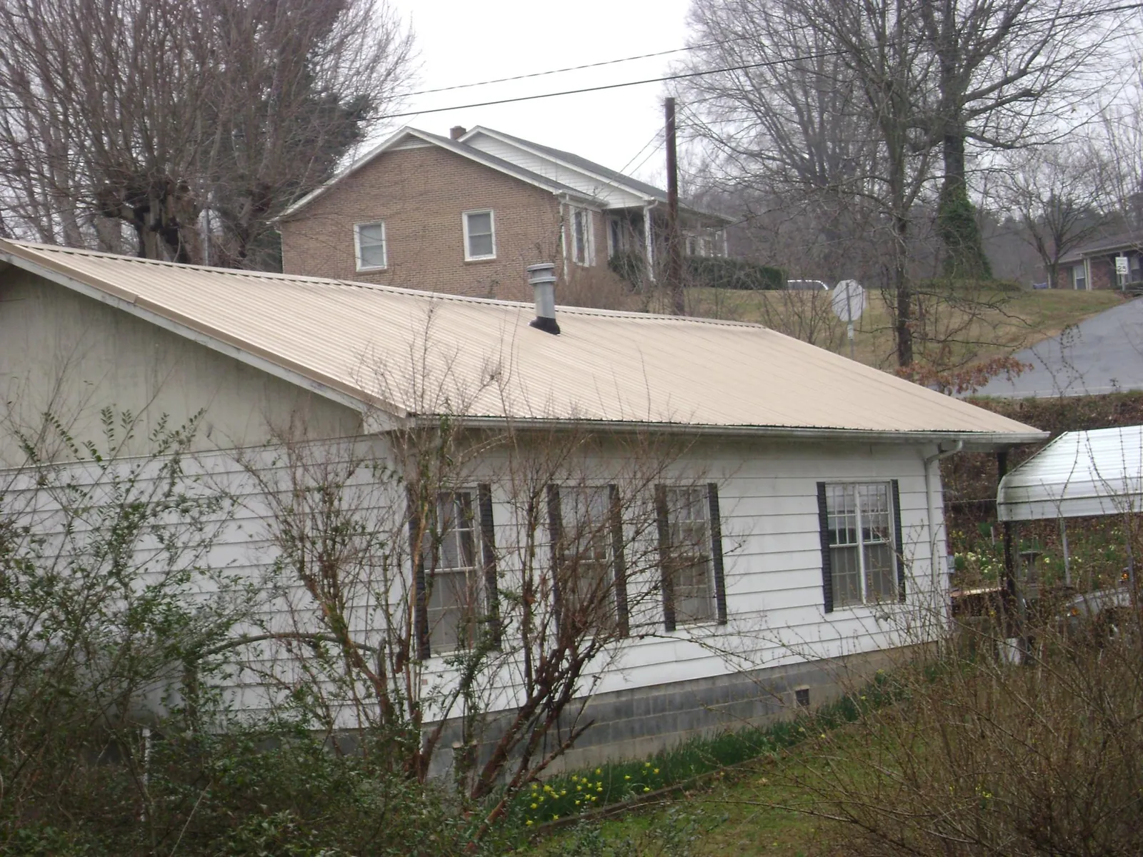 Tan metal roof on a white sided house set into a hillside — Commercial Roofing by Roofing Brothers in West Blocton