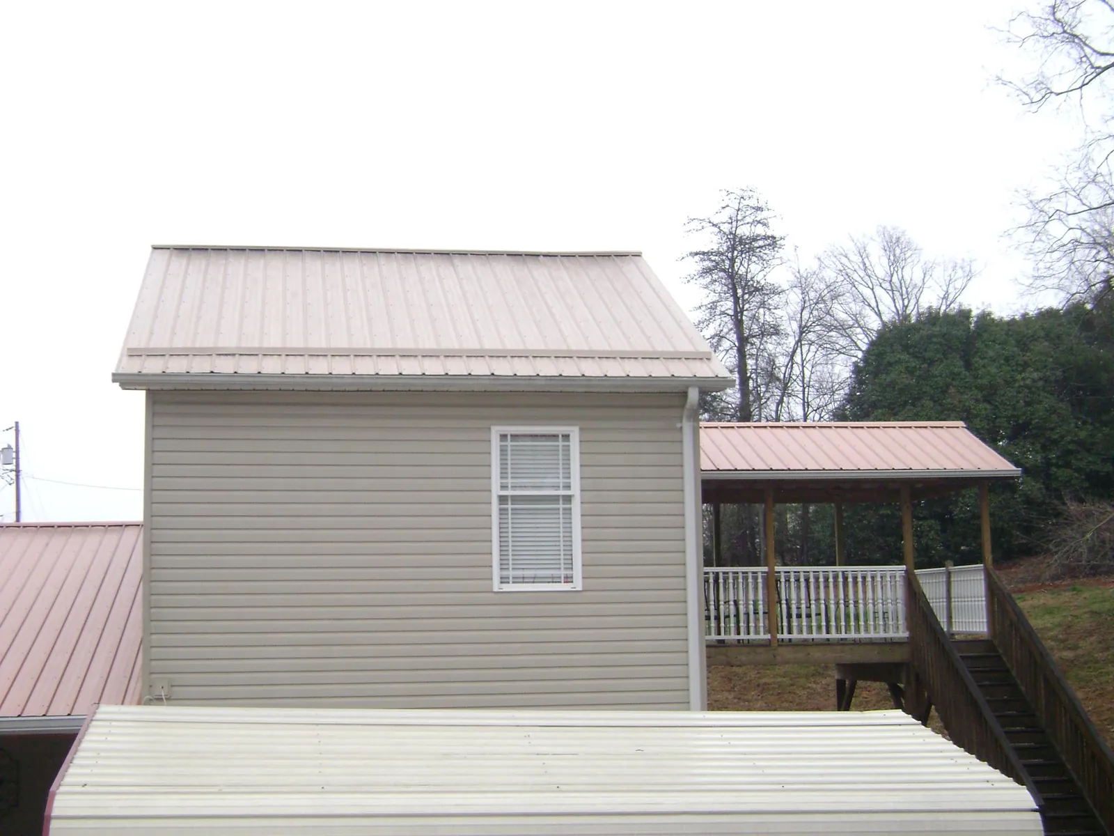 Tan metal roofs on a two story addition and attached porch, from a Roof Replacement job in West Blocton